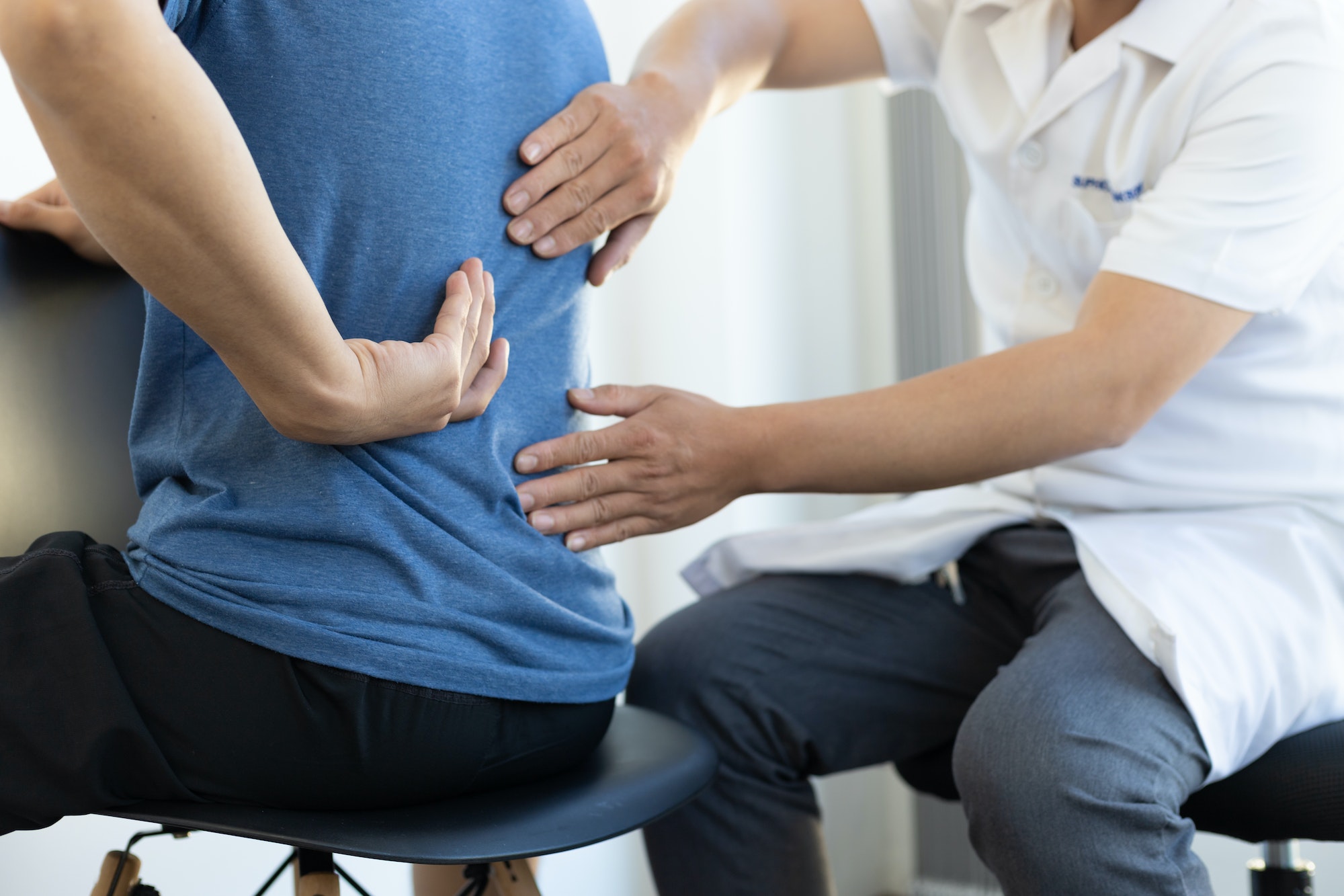 The doctor is diagnosing the patient's back pain. A male with back pain sees a doctor for treatment.